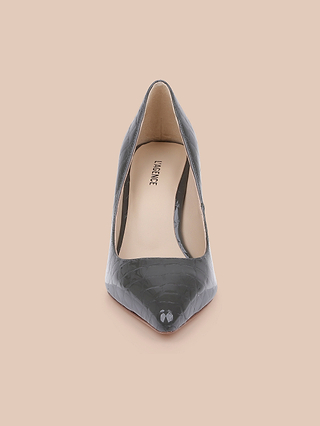 Front view of the Maelle Leather Pump, a single black classic heel featuring a pointed toe, stiletto heel, crocodile-embossed leather texture, and tan insole, shown on a light peach background.
