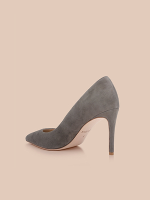 The Maelle Suede Pump in smoke grey showcases a pointed toe and sleek stiletto heel, crafted from suede and set against a soft beige background.