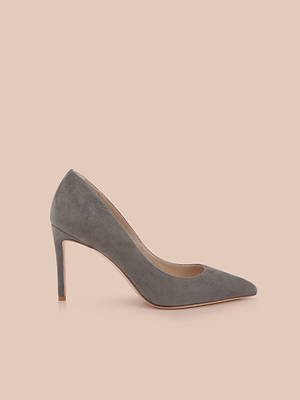 The Maelle Suede Pump is a chic smoke grey stiletto with a pointed toe, elegantly showcased on a light peach background.