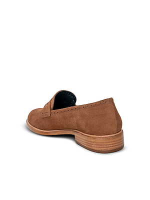 The Avriel Brogue Loafer, a tan suede shoe with an almond toe and low wooden heel, is seen at an angle on a white background. It features subtle perforated detailing near the opening and a sleek, minimalist design.