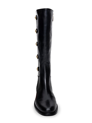 Front view of the L'AGENCE Oceana Riding Boot, a tall black leather design with five gold lion-embossed buttons along the outer side, displayed against a white background.