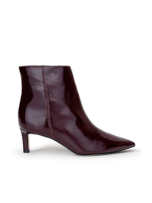The L'AGENCE Lilly Kitten-Heel Bootie is a shiny burgundy patent leather city boot featuring a pointed toe and low, slim kitten heel, pictured in side profile on a white background.