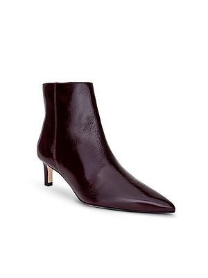 The L'AGENCE Lilly Kitten-Heel Bootie is a glossy dark burgundy patent leather city boot with a pointed toe and low kitten heel, shown against a white background.