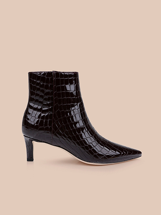 The Lilly Kitten-Heel Bootie, crafted in black crocodile-embossed leather with a pointed toe and kitten heel, is displayed on a beige background.