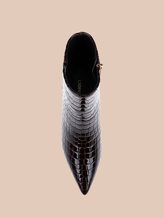 A top view of the Lilly Kitten-Heel Bootie, featuring glossy dark brown crocodile-embossed leather, a pointed toe, and a chic kitten heel, set against a beige background.