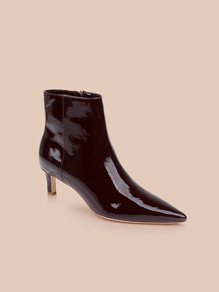 Les bottines Lilly à talon « kitten heel », confectionnées en cuir verni brillant bordeaux foncé, présentent un bout pointu et un talon « kitten heel » bas et fin, et sont présentées sur un fond beige.
