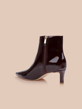 Les bottines à talon bas « Lilly », confectionnées en cuir verni brillant bordeaux foncé, dotées dun bout pointu, dune fermeture éclair latérale et dun talon mi-haut, sont présentées sur un fond beige.