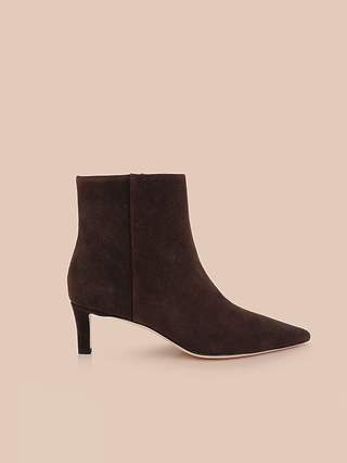 Gli stivaletti Lilly con tacco kitten in pelle scamosciata marrone scuro presentano una punta affusolata e un elegante tacco kitten di media altezza, ripresi di profilo su uno sfondo beige chiaro.