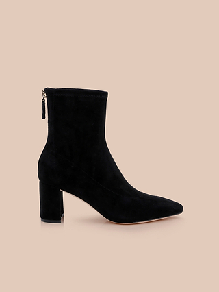 The Salome Stretch Suede Boot, a chic black ankle boot featuring a mid-high block heel and back zipper, is displayed elegantly on a light beige background.