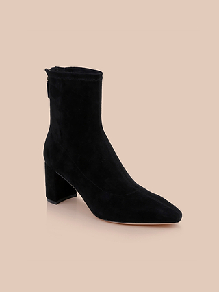 The Salome Stretch Suede Boot is a black ankle boot with a square toe and a mid-height chunky block heel, displayed against a light beige background. This boot features smooth, stretch suede construction, a side zipper for easy wear, and a streamlined silhouette.