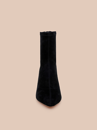 The Salome Stretch Suede Boot in black is positioned upright, facing forward, with its sleek block heel showcased against a plain beige background.