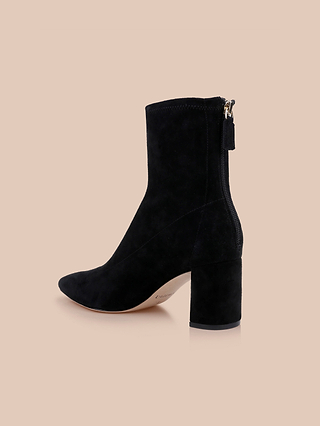 The Salome Stretch Suede Boot, featuring a pointed toe, stylish block heel, and back zipper in black suede, is displayed against a solid beige background.