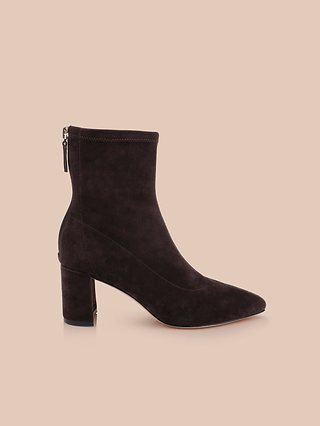 The Salome Stretch Suede Boot, crafted in sleek black suede with a high block heel and a convenient back zipper, is elegantly showcased against a plain beige background.