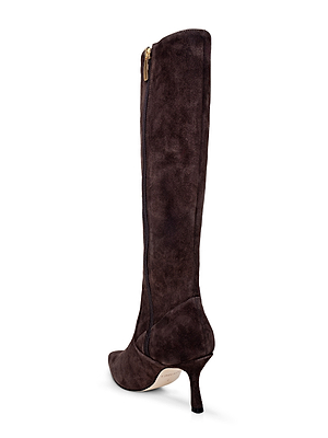 The Marya Knee-High Boot by L'AGENCE is shown from a rear side angle. This dark brown suede boot features a pointed toe, side zipper, slim mid heel, and cushioned memory foam insole against a white background.