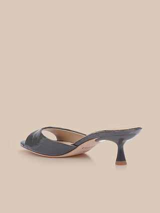 The Arleen Kitten-Heel Mule, featuring a dark gray crocodile-embossed leather upper with open toes, cutout detailing, and a short stiletto heel, is displayed on a light beige background.