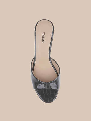 The Arleen Kitten-Heel Mule is a black, open-toe slide sandal crafted from crocodile-embossed leather with a wide textured strap and tan insole, shown from above on a beige background. The LAGENCE logo is printed on the insole near the heel.
