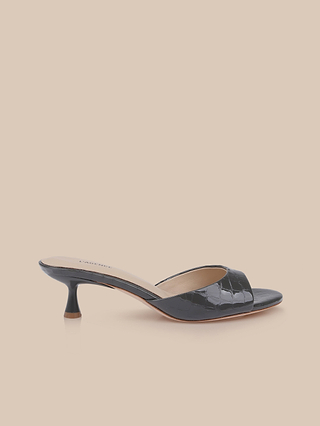 The Arleen Kitten-Heel Mule is a black open-toe sandal crafted from crocodile-embossed leather, featuring a low kitten heel, a memory foam insole, and a neutral backdrop.