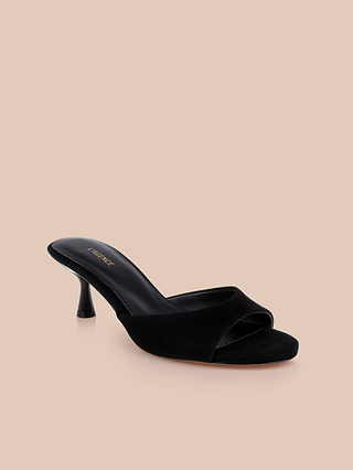 The Arleen Kitten-Heel Mule is a black suede open-toe women’s shoe, showcasing a low kitten heel and a wide front strap for both comfort and style, displayed against a beige background.