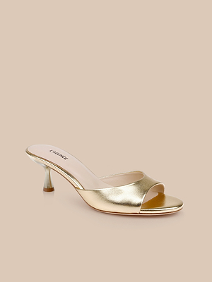 The Arleen Kitten-Heel Mule is a gold leather, open-toe mule with a low clear heel and shiny finish, shown against a beige background.