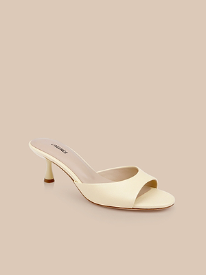 The Arleen Kitten-Heel Mule is a cream-colored, open-toe shoe with a low kitten heel and minimalist design, made from smooth yellow leather and shown on a beige background.