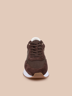 The Deepa Platform Sneaker, featuring chocolate suede and mesh, is displayed front-facing against a beige background, showcasing its toe, laces, partial white sole, and plush memory foam insole.