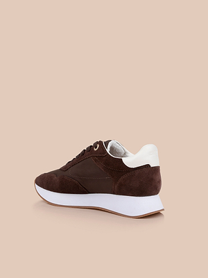 The Deepa Platform Sneaker features chocolate suede and leather with white accents, a chunky white sole, and memory foam insole, shown angled on a beige background.