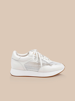 The Deepa Platform Sneaker showcases an all-white leather construction with mesh panels, complemented by white laces and a chunky white sole. Finished with a supportive memory foam insole, this sporty sneaker is displayed against a neutral beige background.
