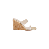The Farrell Wedge Espadrille is a raffia wedge sandal with a woven straw heel and two clear vamp straps across the foot, shown in side profile on a white background. This stylish design is completed with a modern square toe.