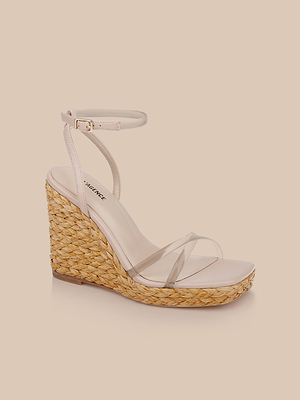 The Malone Wedge Espadrille features a beige design with a woven straw heel, clear square-toe strap, and thin buckled ankle strap, shown against a light peach background.