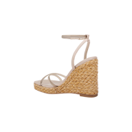 The Malone Wedge Espadrille is a beige strappy sandal with a high raffia wedge heel crafted from woven straw, featuring an ankle strap and a slightly open toe, shown against a white background for an effortless bohemian style look.