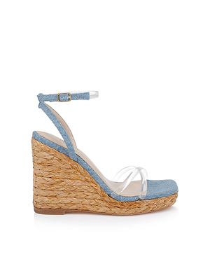 The Malone Wedge Espadrille features denim, a woven straw heel, transparent toe straps, and an adjustable buckle ankle strap, shown against a white background.