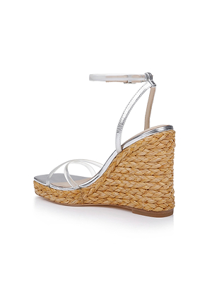 The Malone Wedge Espadrille is a silver strappy sandal with a high braided raffia wedge heel and ankle strap, shown on a white background at an angle highlighting the side and back.