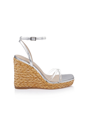 The Malone Wedge Espadrille features a braided raffia wedge heel, metallic silver ankle strap, and two clear front straps, shown as a single sandal against a white background.