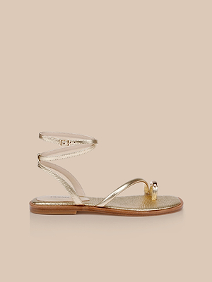 The Mariana Leather Sandal features gold lizard-embossed leather, a thin ankle tie strap, toe loop, and tan sole, shown against a plain beige background.