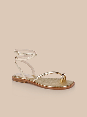 The Mariana Leather Sandal features gold lizard-embossed leather, an ankle strap, delicate toe loop, and a thin sole with a brown edge, shown against a beige background.