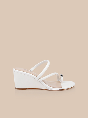 The Maritza Wedge Sandal features a white leather upper, two thin straps, a metal-capped toe ring accent, and a walkable wedge heel. This open-toe style is shown from the side on a beige background.