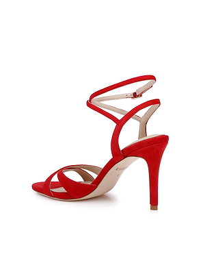 The Miranda Suede Sandal is a red high-heeled shoe featuring open toes, crisscross straps, and a thin buckle ankle wrap. Its slender heel is covered in matching suede, making it ideal for evenings or special occasions.