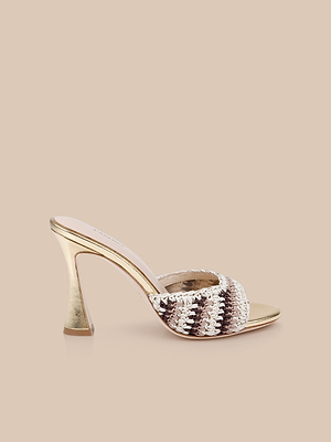 The Moyes Crochet Sandal features a stylish gold crochet design with a flared sculpted heel and a wide, woven strap in metallic gold and beige tones, displayed on a neutral beige background.