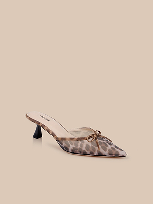 The Palermo Mesh Mule features a pointed toe, slip-on design, sheer leopard print mesh upper, black low sculpted heel, and a small bow on top, shown against a beige background.
