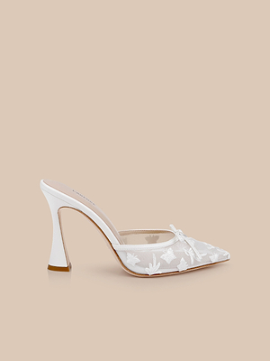 The Prasad Mesh Mule is a white mesh mule with a pointed toe, floral and butterfly embroidery, plus a bow detail, shown on a light beige background.