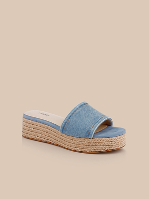 The Ramani Platform Espadrille is a blue denim slide sandal with an open toe and jute-wrapped platform sole, ideal for spring and summer, shown on a light beige background.