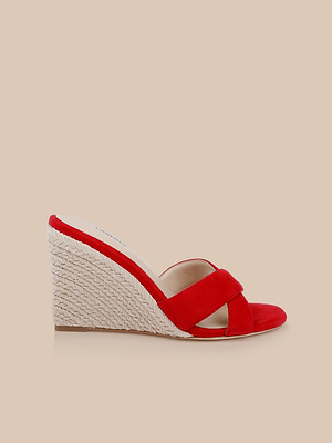 The Rosaline Wedge Espadrille is a red suede sandal with crisscross straps and a woven straw platform heel, ideal for womens summer footwear, shown on a beige background.