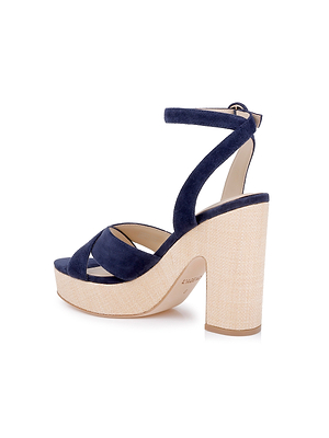 The Sandrine Platform Sandal features navy suede crisscross toe straps, a closed back with buckle, and an ankle strap for support. Set on a thick, beige raffia-wrapped wedge heel, this stylish high-heeled design is both chic and comfortable.