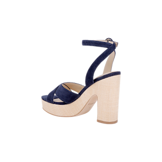 Introducing the Sandrine Platform Sandal: a chic footwear choice featuring a thick beige heel and platform, complemented by navy blue suede crisscross straps and an adjustable ankle strap with buckle. Set against a white background, this modern design is inspired by the look of a raffia-wrapped wedge, offering unique textural appeal.
