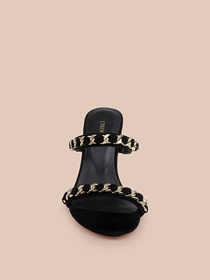 The Sarika Chain Sandal is a black suede open-toe heel featuring two straps with bold chain hardware, displayed on a plain beige background—a true high-fashion statement.