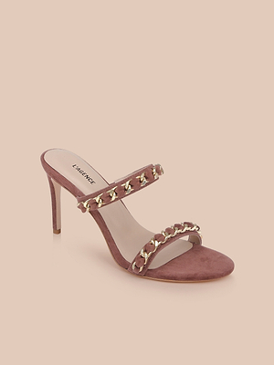 The Sarika Chain Sandal is a mauve high-fashion shoe with two gold chain-adorned straps, an open toe, and a suede stiletto heel, shown on a light beige background.