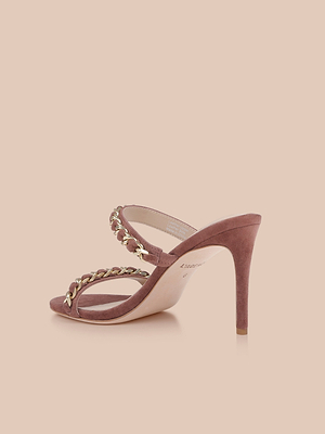 The Sarika Chain Sandal is a mauve high-heeled sandal with a suede heel, featuring two thin straps embellished with gold chain detailing across the front, displayed on a light beige background.
