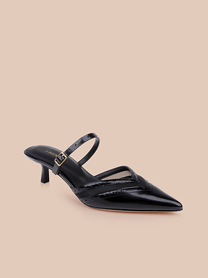 The Shelbie Kitten-Heel Mule features black leather, a pointed toe, low kitten-heel, thin crisscross straps, and an ankle buckle, shown on a beige background.