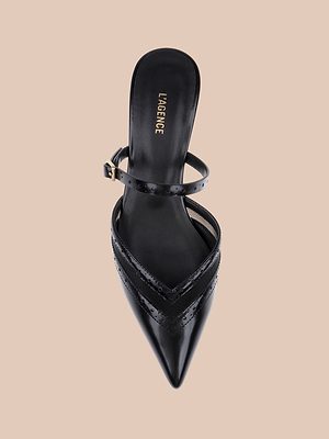 The Shelbie Kitten-Heel Mule is a black leather pointed-toe mule with an ankle strap, glossy finish, and kitten heel, shown from above on a beige background. LAGENCE branding is visible on the insole.