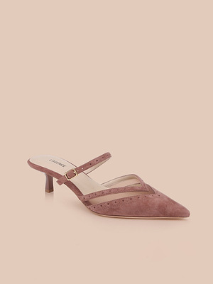 The Shelbie Kitten-Heel Mule features pink suede, a pointed toe, low kitten heel, and a thin strap with gold buckle. Brogue details and perforated accents add elegance, showcased on a neutral beige background.